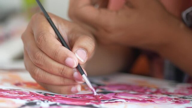 Close up of artist hand painting with small brush on colorful canvas with pink and red shades