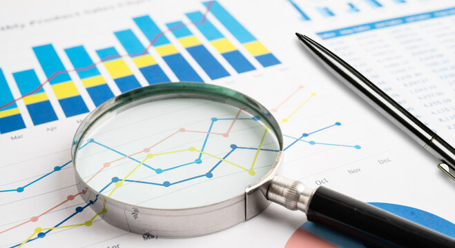Magnifying glass examining financial charts and business graphs with a black pen on a desk magnifying financial