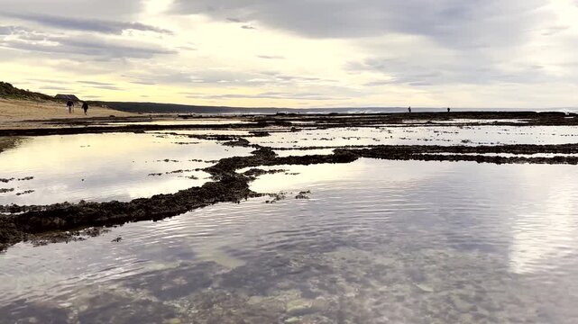 Scenic coastal landscape with shallow rock pools during low tide at sunset.