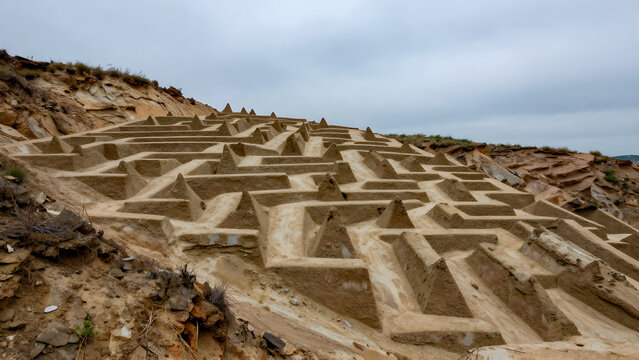 Ancient stepped earthwork structure on a hillside under cloudy sky