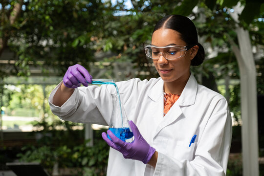 Young woman scientist performing a chemical experiment in a greenhouse setting