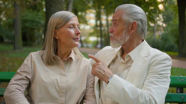 Close up of happy Caucasian elderly couple sitting on park bench laughing talking hugging cheerful senior man woman aged family enjoying carefree retirement relaxation weekend rest together outdoors