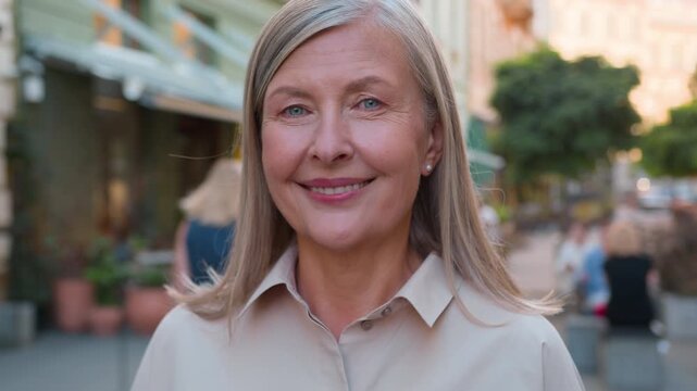 Close up portrait of happy elderly gray haired Caucasian woman smiling at camera on city street elegant retired businesswoman joyful senior female tourist enjoying carefree life travel holiday outdoor