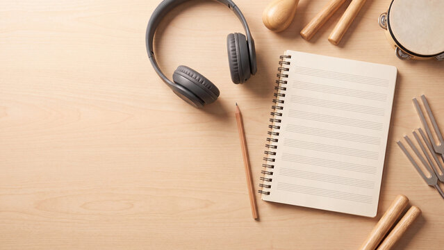 Notebook lies flat beside dark headphones and wooden musical percussion instruments on a smooth desk.