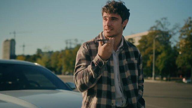 Caucasian smiling business man recording voice message on mobile phone near luxury car in city happy male businessman driver sending audio voicemail talking on speakerphone outdoors modern automobile