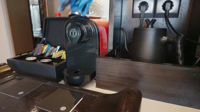 Modern coffee capsule maker and electric kettle on countertop in hotel room.