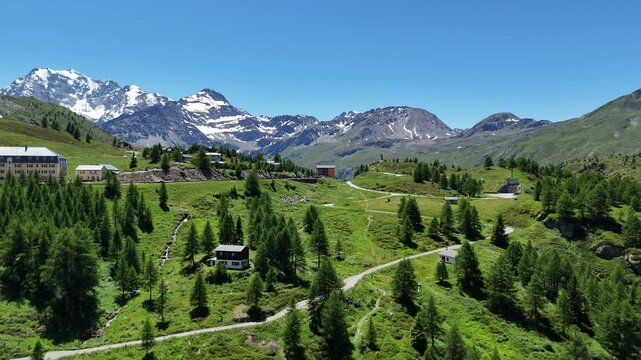 Aerial view of the scenic Simplon Pass in the Swiss Alps during summer, featuring winding mountain roads, green alpine slopes and dramatic peaks under a clear blue sky.