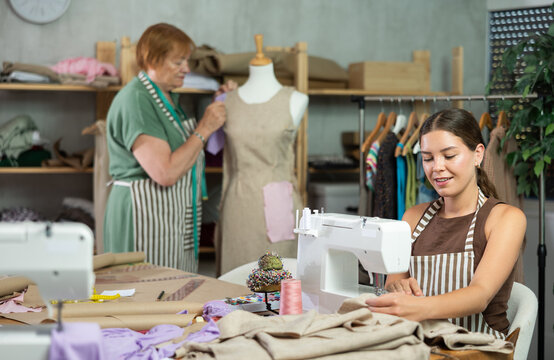 Seamstress works on a sewing machine and stitches fabric against the background of an experienced dressmaker who works with a mannequin. Team of dressmakers sews custom-made clothes in the workshop