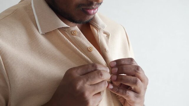 A man carefully unbuttoning his shirt with precision, showcasing the textured fabric and meticulous actions in a close-up indoor video