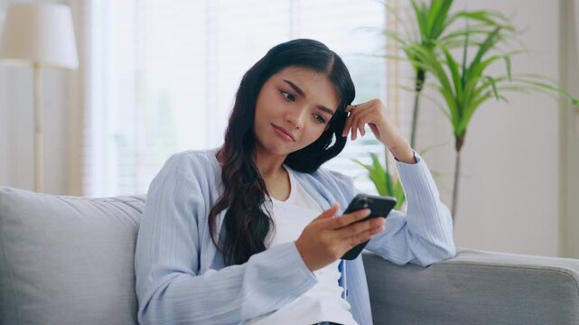 Happy young asian woman relax on comfortable couch at home texting messaging on smartphone, smiling girl use cellphone, chatting online message, shopping online from home