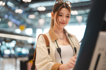 Asian woman traveler woman using self service check in counter kiosk machine for boarding pass...