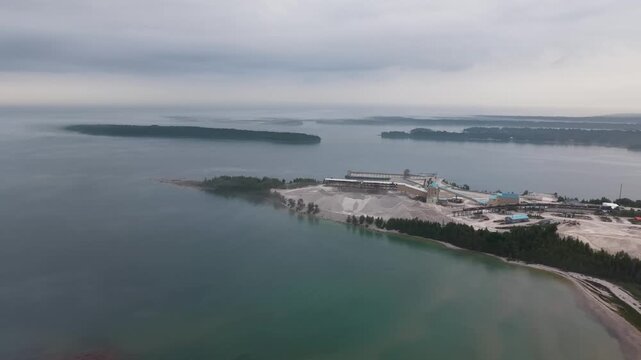 Drone footage sweeps over curving bays low islands and calm coastal water beneath a cloudy Upper Peninsula sky