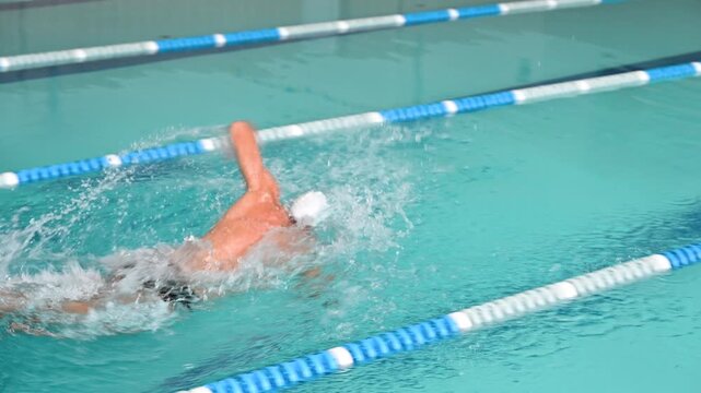 Side view of man swimming freestyle crawl in indoor pool. Sports video captures alternating arm stroke, flutter kick, and steady forward motion during lap training
