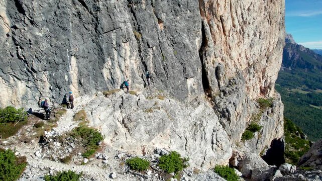 Via ferrata climbers traverse exposed rocky ledge on Michielli-Strobel route in Dolomites, Italy, using safety cable while moving along steep mountain wall during alpine adventure