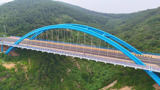 Aerial orbit view of the Jinshitan Blue Bridge spanning the Yellow Sea near Dalian, Liaoning, northeastern China, showcasing the coastal landscape and turquoise waters.