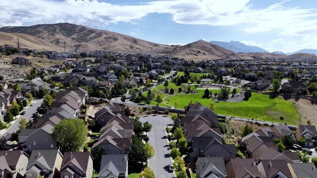 Drone video showcases Travers Mountain&rsquo;s modern suburban homes, landscaped streets, green park areas, and dramatic mountain backdrop under bright daylight, revealing Lehi, Utah's urban edge.