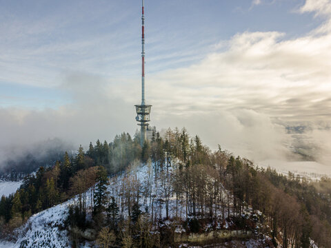 Bantiger TV tower on snow-covered hill - aerial winter panorama over Ittigen with misty clouds and forested slopes