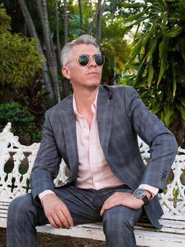 Elegant Man in Suit and Sunglasses Sitting on a Park Bench