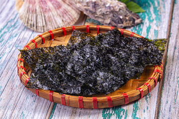 Dark nori seaweed sheets in woven bamboo basket on rustic wooden surface © Andrei Starostin