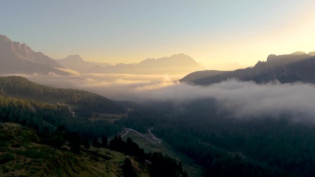 Witness the stunning colors of dawn illuminating the clouds and mountains at Passo Giau, Dolomites Italy. This serene landscape promises an unforgettable experience for all nature lovers.