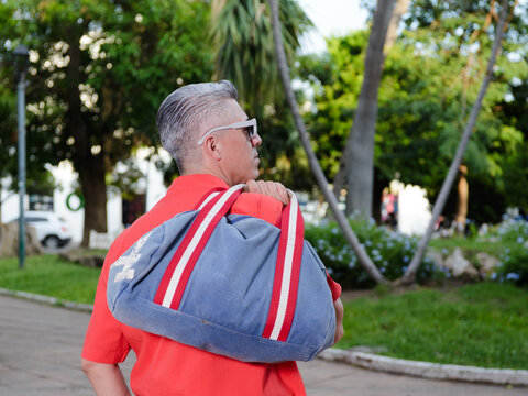 Man with White Sunglasses and Backpack Walking Through a Public Park