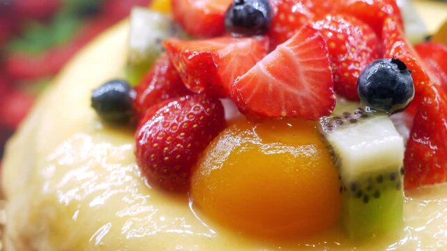 Close up motion of delicious fresh fruit cake with glossy glaze, featuring strawberries, blueberries, kiwi, and peach, vibrant dessert footage