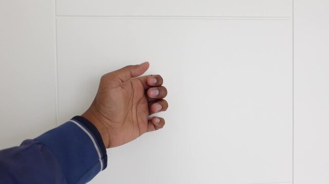 Close-up cinematic footage of dark-skinned hand knocking on white wooden door repeatedly