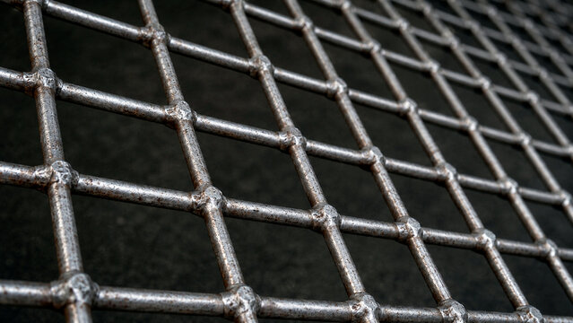 heavy duty metal wire mesh grid with visible welds. Industrial steel grating texture with rust spots. Selective focus on geometric pattern