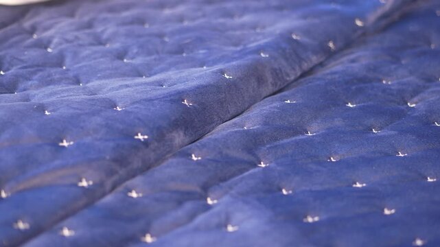 Close up on blue quilted fabric texture with small white stitches moving slowly