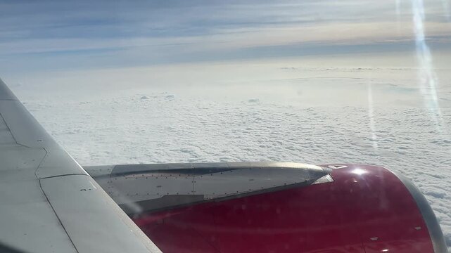Aerial view from passenger window over white cloud layer during flight above airplane engine.