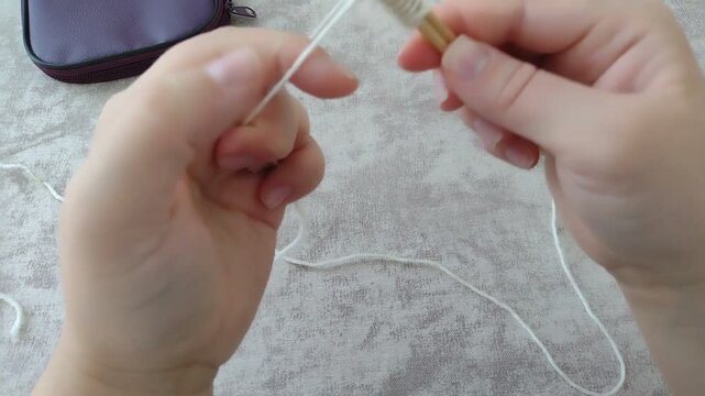 Hands casting on stitches onto wooden knitting needles using white yarn over a textured table. Horizontal stock footage for knitting tutorials, DIY crafts, handmade hobbies, and craft vlogs.