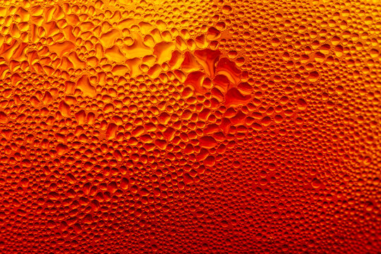 Macro water droplets condensation on cold amber glass background,A detailed macro photograph capturing water condensation droplets on a cold glass surface illuminated with warm amber and orange.