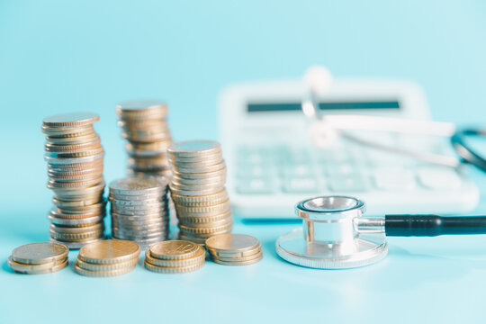 Stacks of coins beside a stethoscope and calculator on blue background, illustrating healthcare costs, medical expenses, insurance budgeting, hospital bills, payment planning,