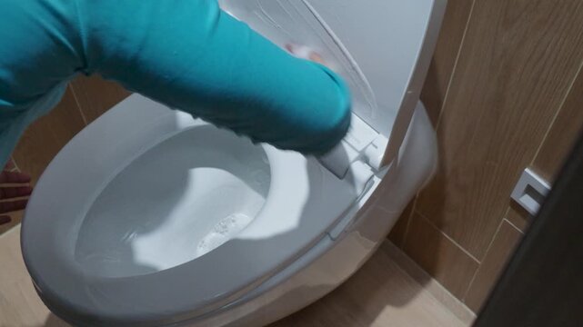 Person cleaning and wiping a white toilet bowl seat in a modern bathroom.