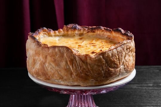 Golden Brown Flaky Pie on Vintage Pink Glass Stand Against Burgundy Curtain