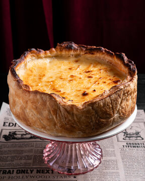 Golden Brown Flaky Pie on Vintage Pink Glass Stand Against Burgundy Curtain