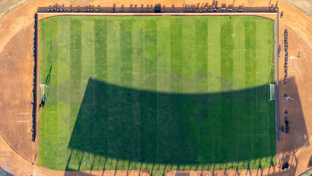 Aerial view of a soccer field with a large shadow cast across the green grass and surrounding dirt track in Bantul, Special Region of Yogyakarta, Indonesia.