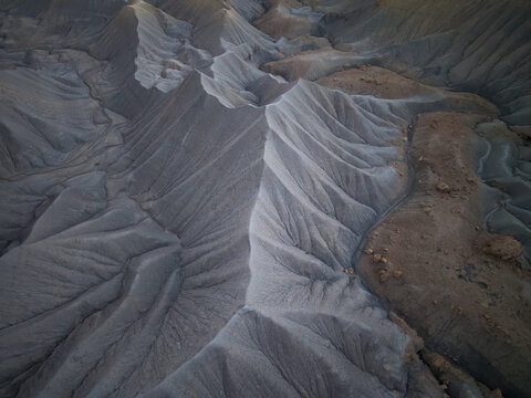 Aerial view of the rugged badlands of Caineville Mesa featuring sharp ridges, deep erosion patterns, and contrasting earth tones in Wayne County, Utah, United States.