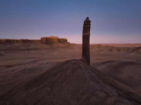Aerial view of the unique rock formation rising from the rugged desert landscape with eroded sandstone hills and a soft twilight sky in Hanksville, Utah, United States.