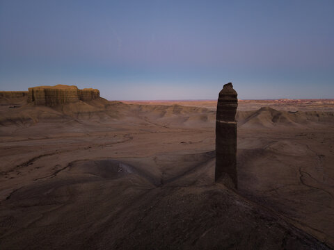 Aerial view of a solitary rock spire rising from the desert floor with a distant mesa under a soft twilight sky in Hanksville, Utah, United States.