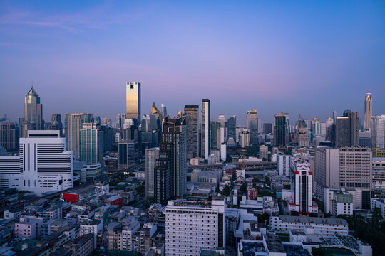 Aerial view of the Bangkok skyline featuring modern skyscrapers, dense urban architecture, and city streets under a clear twilight sky in Bangkok, Bangkok, Thailand.