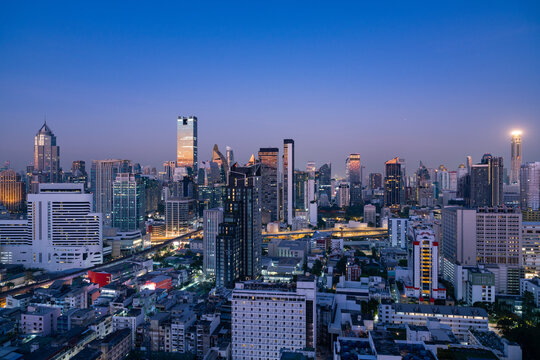 Aerial view of the modern Bangkok skyline at dusk with illuminated skyscrapers, dense urban architecture, and glowing city lights in Bangkok, Bangkok, Thailand.