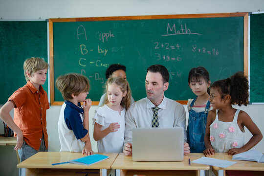 International school teacher and diverse elementary students gather around laptop for technology learning, digital education and collaborative classroom activity.
