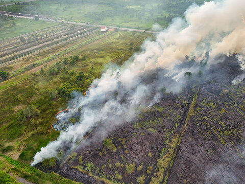 Aerial view of a wildfire burning in a field with thick smoke rising over the landscape in Indonesia.