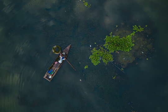 Aerial view of a fisherman in a small wooden boat navigating through water hyacinths on Lake Rawa Pening in Waduk Rawapening, Central Java, Indonesia.