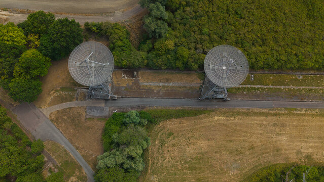 Aerial view of the Mullard Radio Astronomy Observatory featuring two large radio telescope dishes in a rural landscape with trees and fields in Harlton, England, United Kingdom.