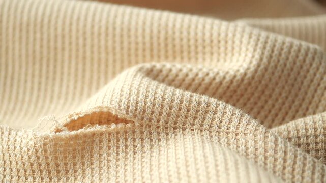 Macro view of damaged beige thermal fabric with visible hole and frayed threads in slow motion
