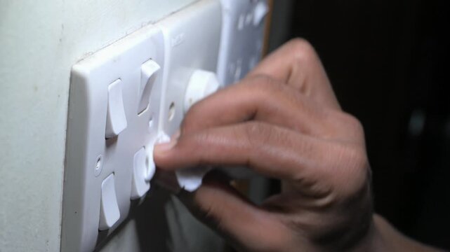 A person uses a tissue to switch on and off a white light switch on a wall, demonstrating how to prevent contact with surfaces to avoid illness