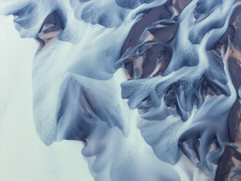Aerial view of the intricate glacial river patterns flowing near Naustavik Mountain, showcasing dark volcanic sediment contrasting with bright glacial silt in Husavik, Nordurthing, Iceland.