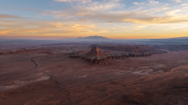 Aerial view of Wild Horse Butte rising above the vast desert landscape of the San Rafael Swell at sunset with soft golden light illuminating the rugged terrain, Green River, Utah, United States.